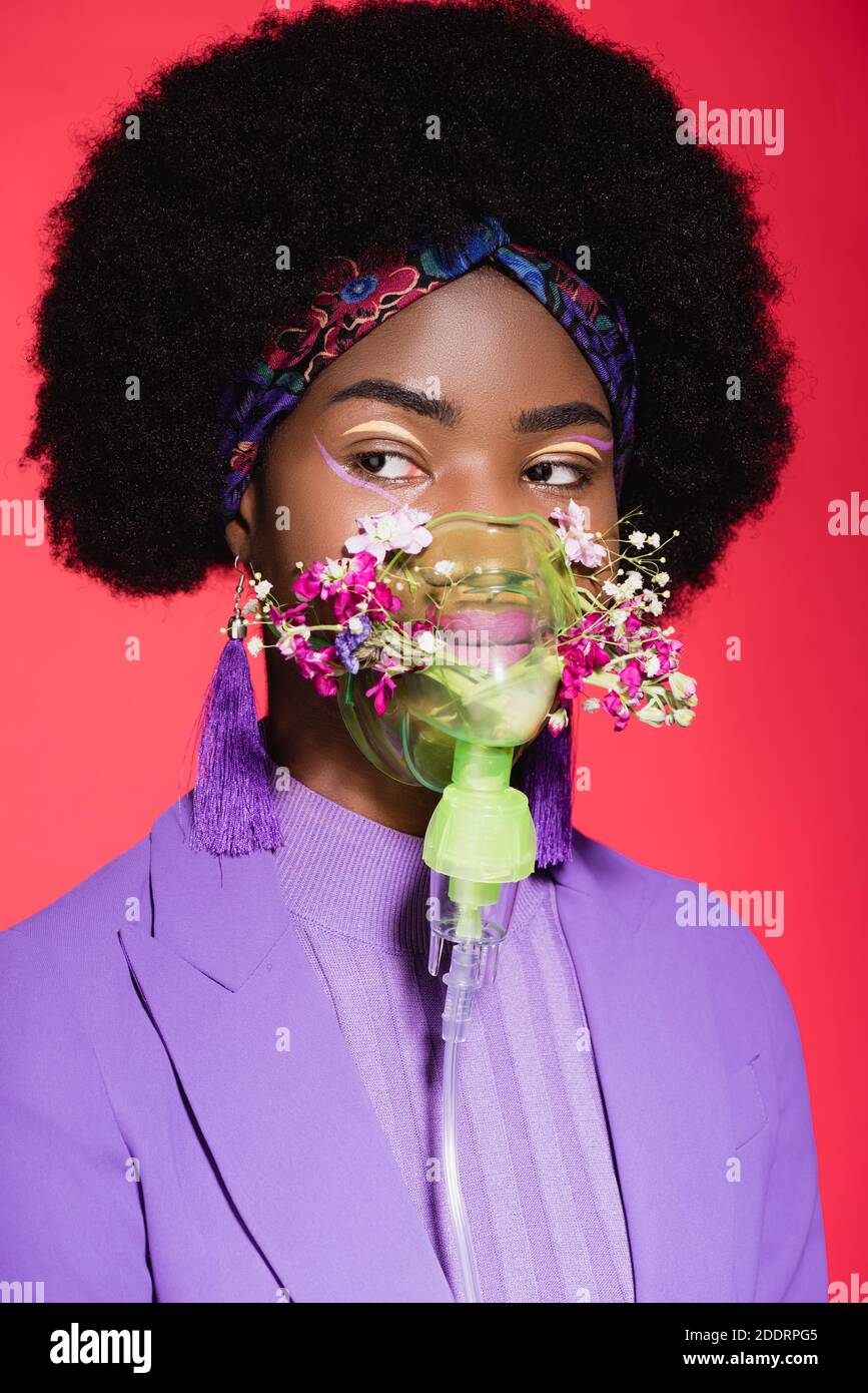mujer joven afroamericana en traje púrpura con estilo y flores en inhalador aislado en rojo Foto de stock