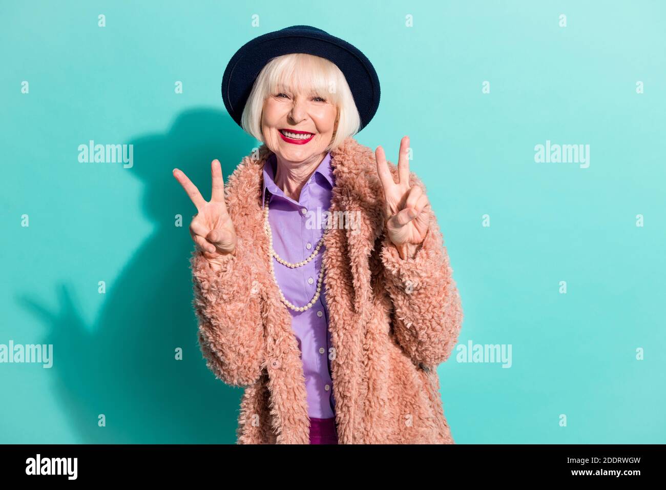 Foto de la brillante graciosa señora mayor llevar brazos chaqueta retro  ropa de cabeza que muestra el signo v aislado color verde azulado fondo  Fotografía de stock - Alamy