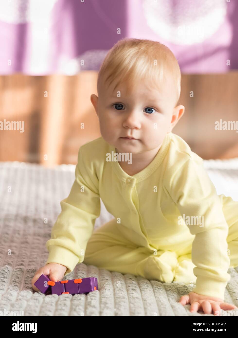 Un bebé que se cría con ropa amarilla se sienta en un ambiente hogareño. En  las manos de un rompecabezas púrpura Fotografía de stock - Alamy