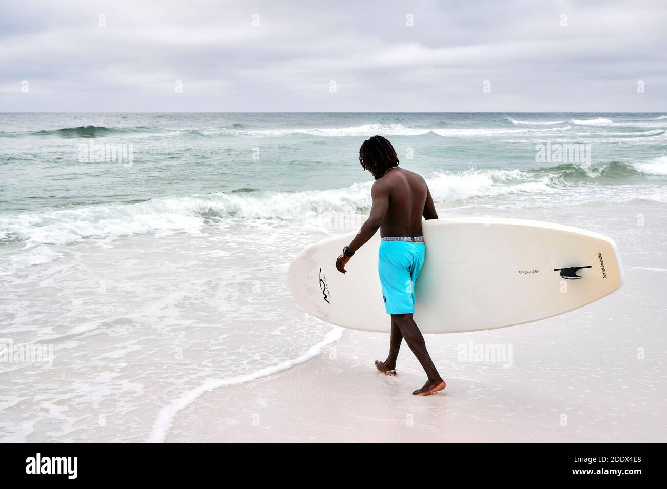 Hombre negro, afroamericano, surfista llevando una tabla de surf en el Golfo de México en la panhandle de Florida USA. Foto de stock