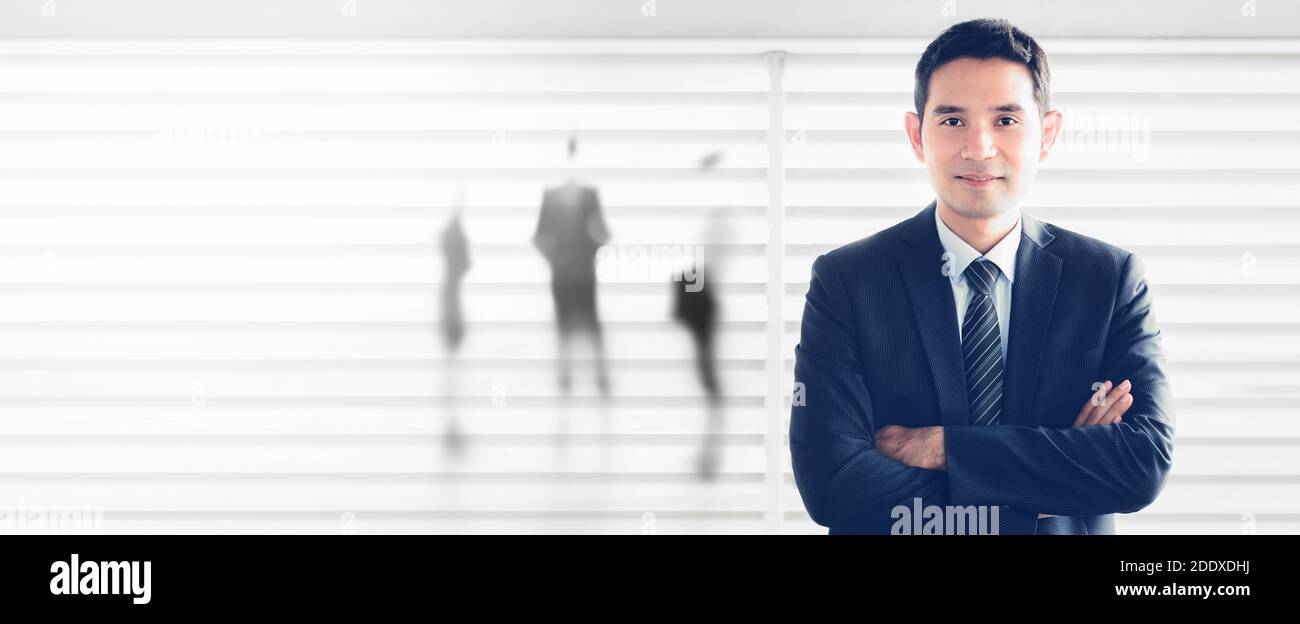 Joven empresario asiático sonriendo mientras cruza sus brazos en la ventana blanca de fondo de la oficina, pancarta panorámica - líder y empresario de éxito conceph Foto de stock