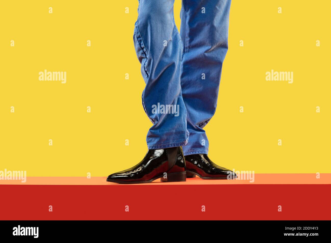 Las piernas de un joven hombre de moda en pantalones vaqueros azules y  botas negras en el piso rojo Fotografía de stock - Alamy