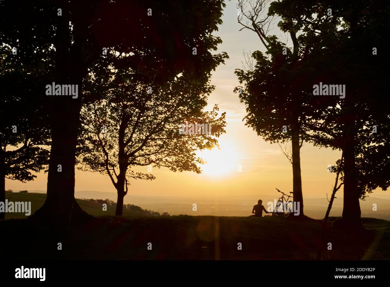 Un hombre con bicicleta observa una puesta de sol en la cima de una colina en South Downs Way, Inglaterra, Reino Unido Foto de stock