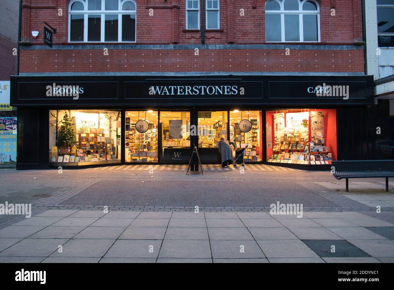 Una persona mayor sola lee un cartel fuera de una sucursal cerrada del librero del Reino Unido Waterstones en una calle alta en declive en el noroeste del Reino Unido. Foto de stock