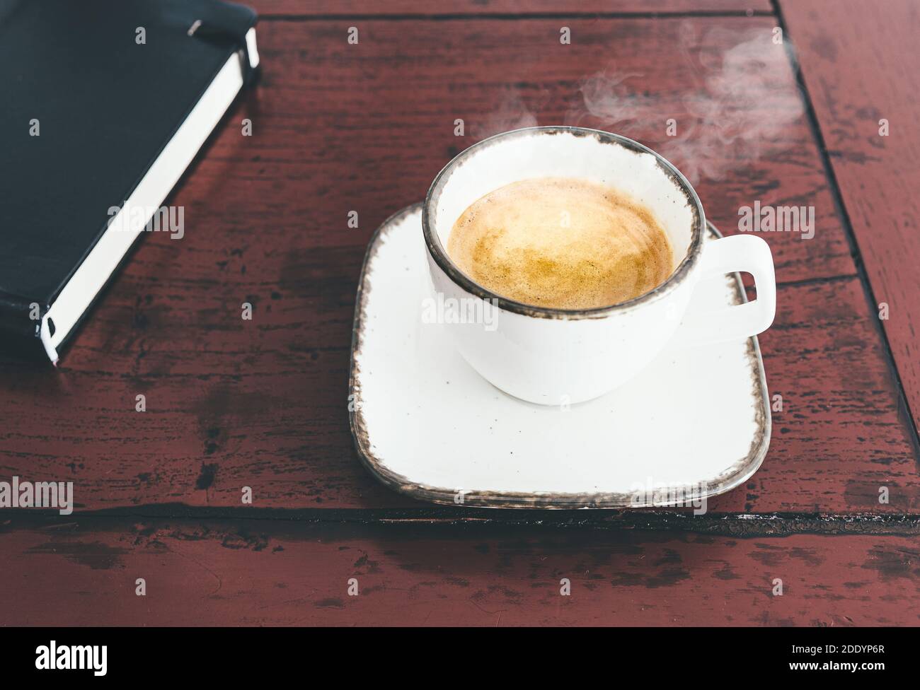 primer plano de una taza de expreso caliente al vapor sobre madera rústica escritorio con libro Foto de stock