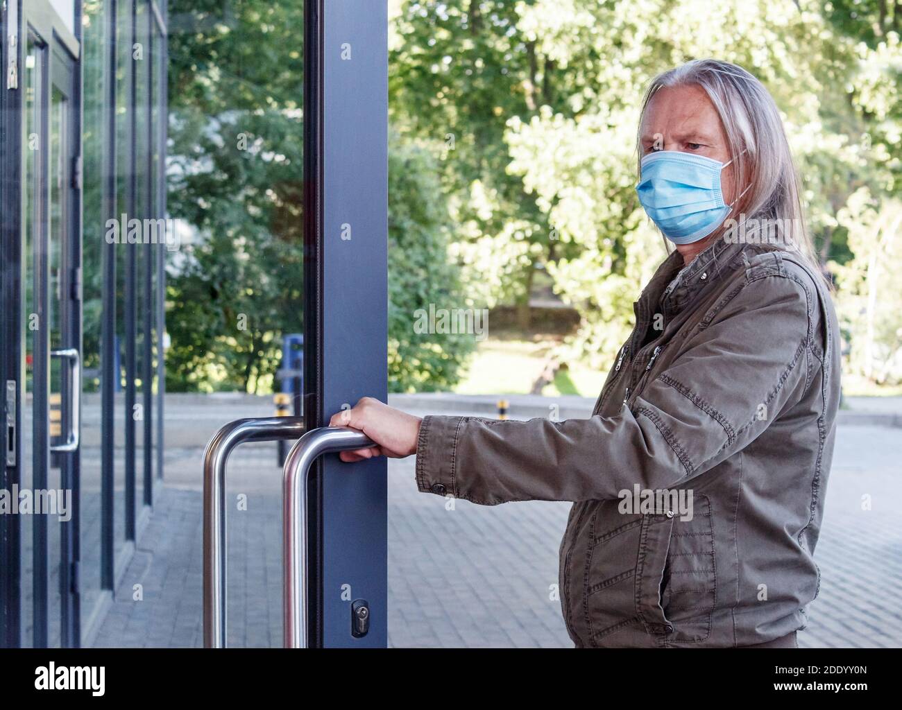 el anciano con máscara protectora abre la puerta del tienda al aire libre el día de otoño Foto de stock