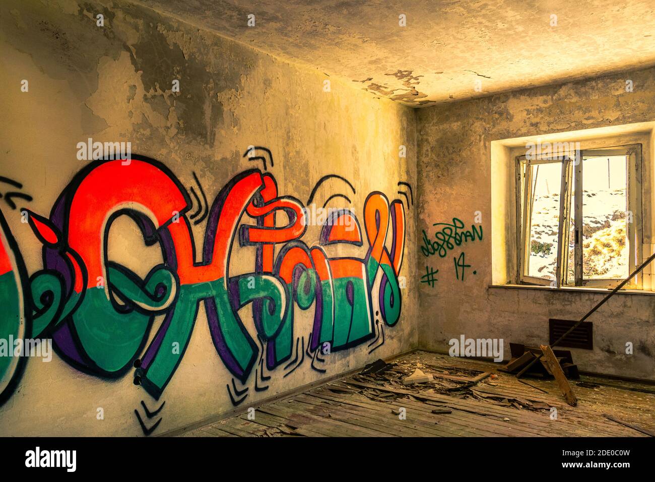 Habitación desbocada con ventana rota, suelo de madera destruido, paredes de graffiti multicolores. Interior de edificio abandonado. Monte Grappa, Vicenza, Italia Foto de stock