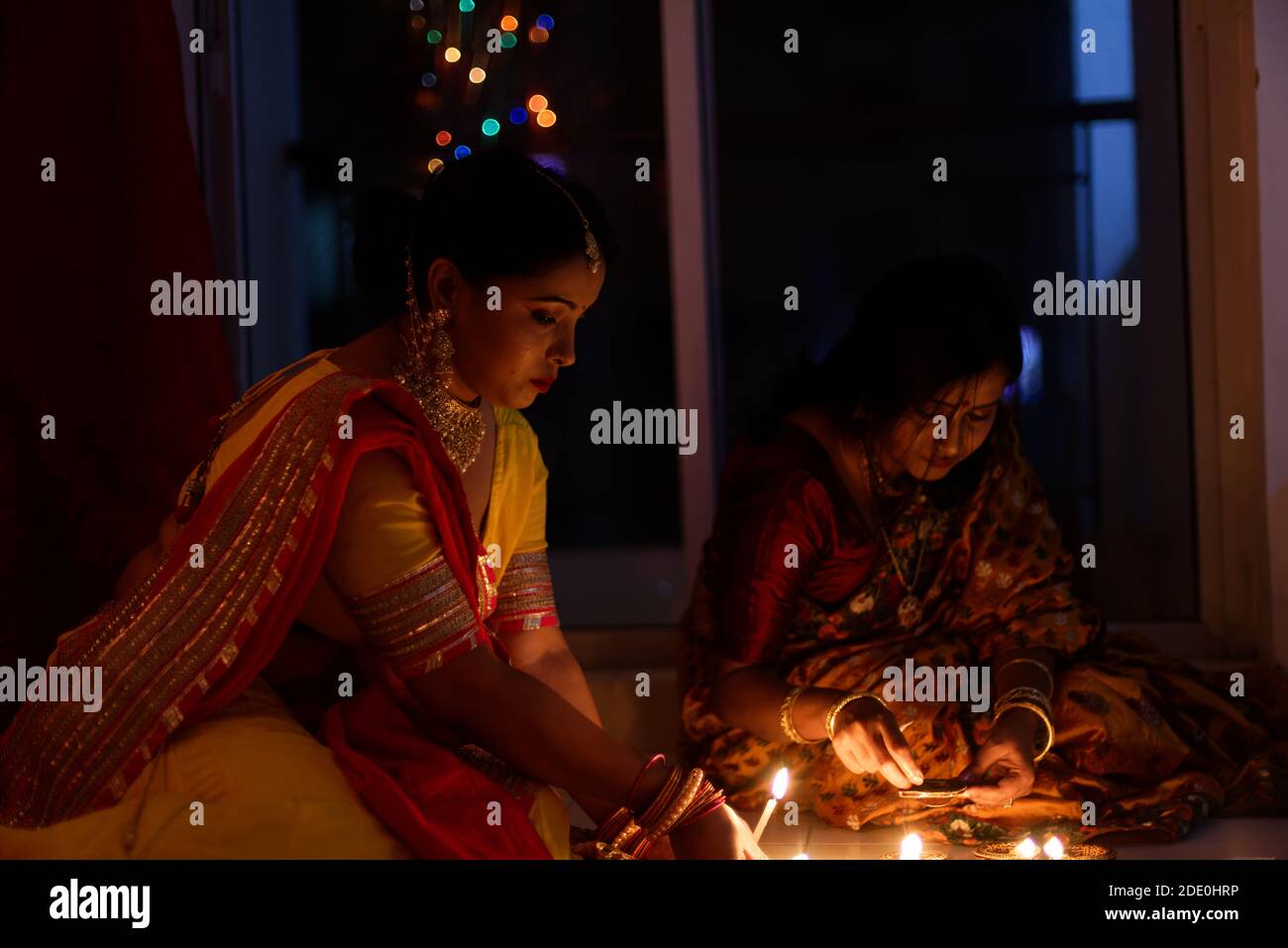 Dos hermosas mujeres bengalíes de la India en traje tradicional de iluminación Diwali diya / lámparas sentado en el suelo en la oscuridad en la noche de Diwali. Foto de stock
