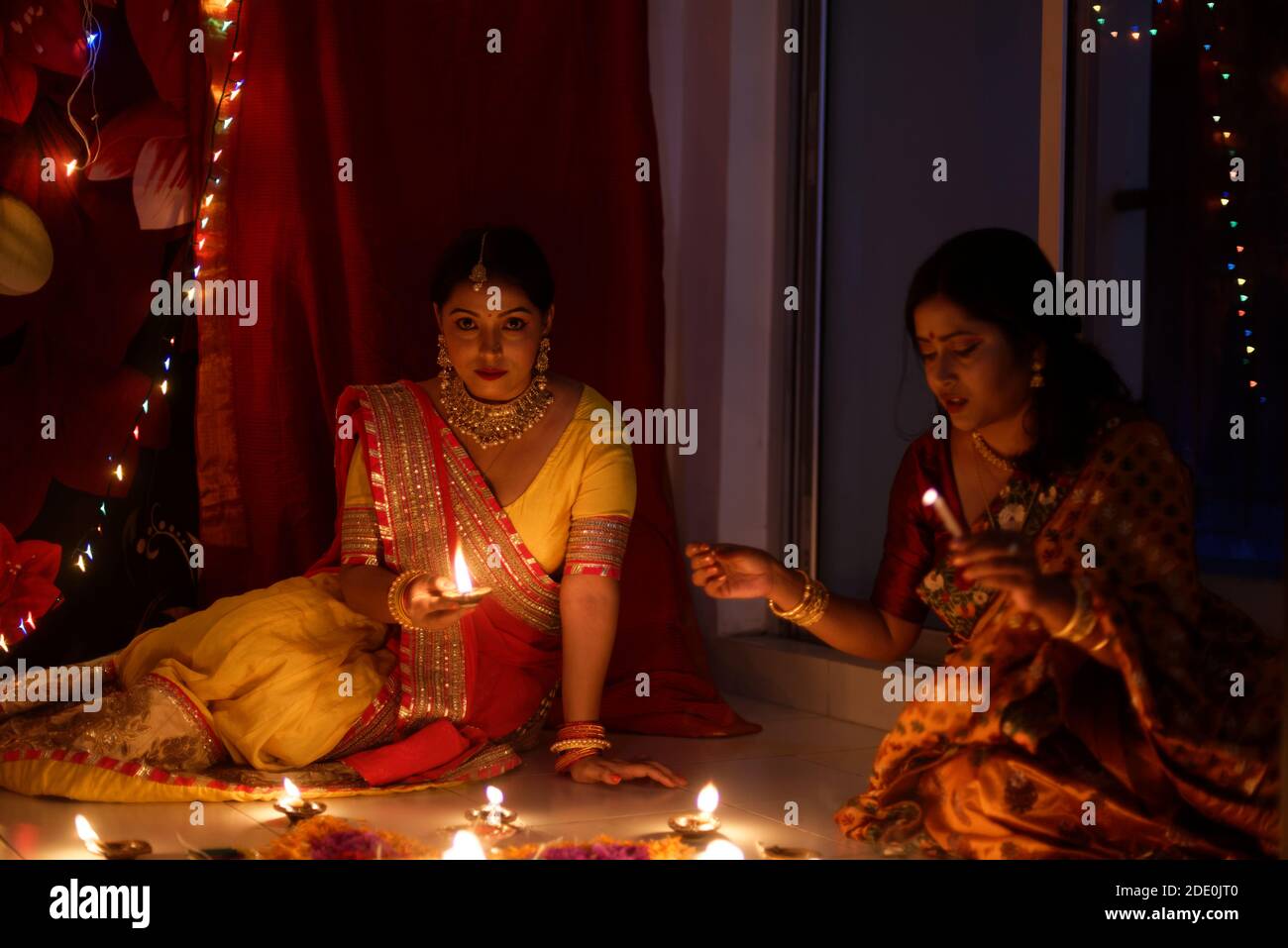 Dos hermosas mujeres bengalíes de la India en traje tradicional de iluminación Diwali diya / lámparas sentado en el suelo en la oscuridad en la noche de Diwali. Foto de stock