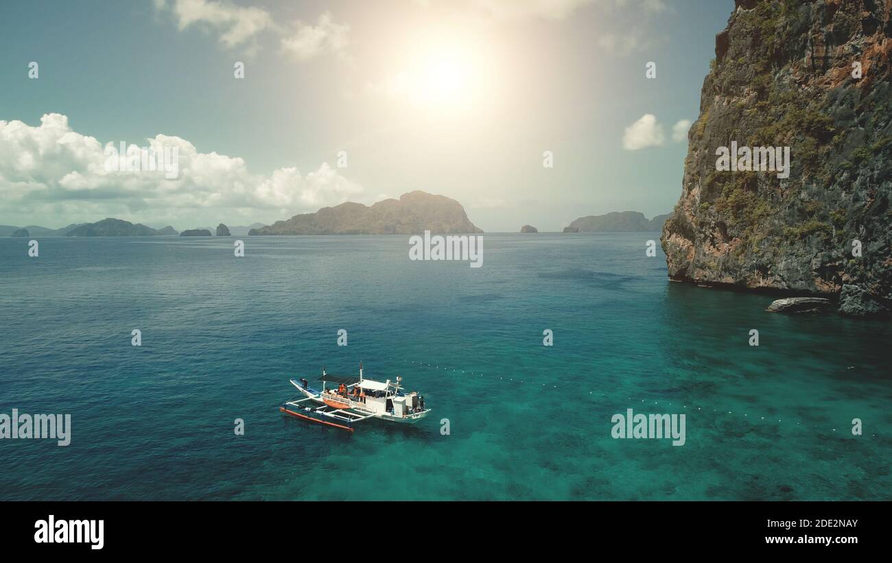 Primer barco de pasajeros en la costa del mar con verde acantilado en vacaciones de verano día del sol. Sereno paisaje marino tropical en la isla de montaña de Filipinas, archipiélago de Visayas. Primer plano cinematográfico de drone Foto de stock