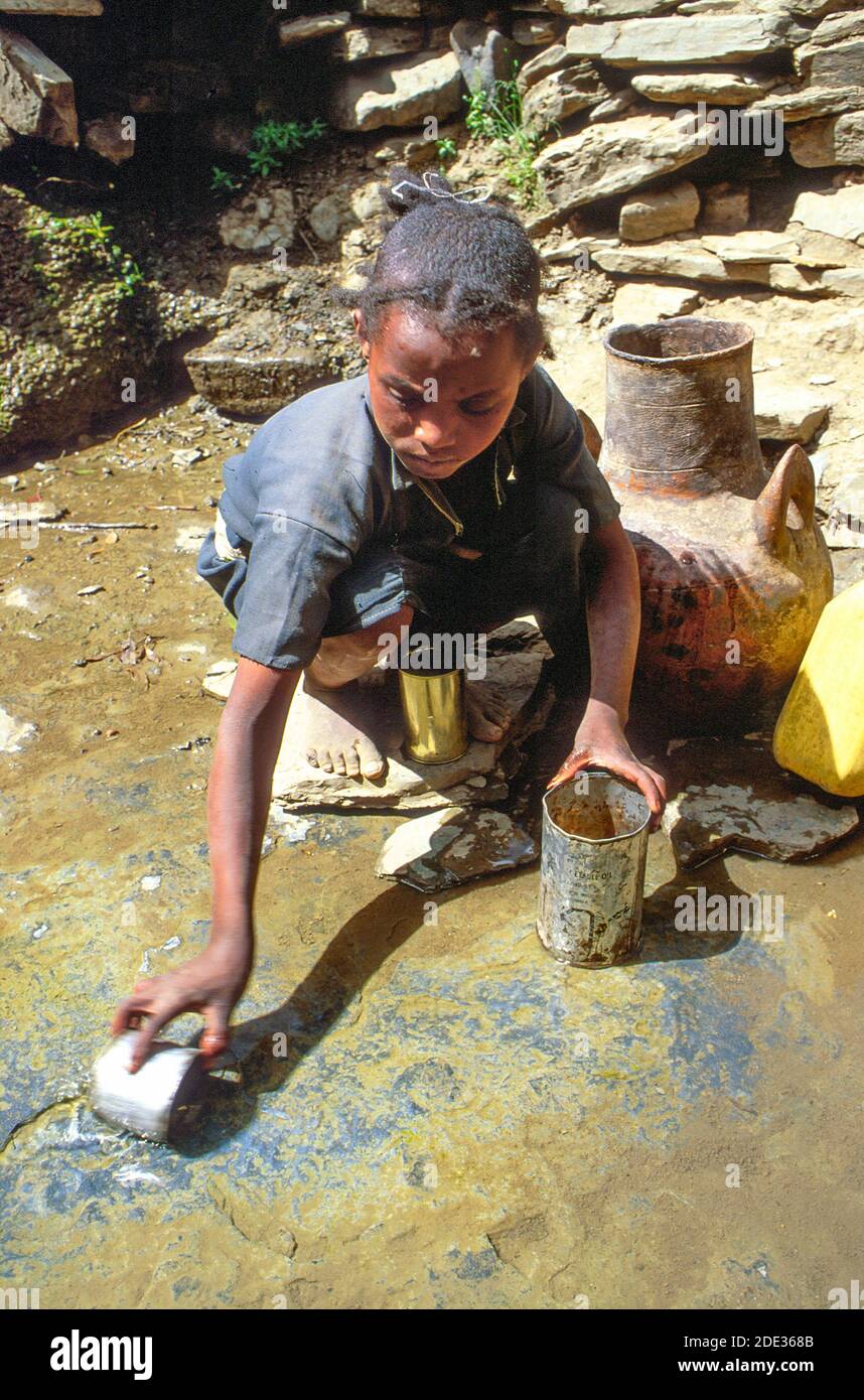 Una niña pequeña que toma agua en una lata de una fuente de agua insegura. Tigray, Etiopía Foto de stock