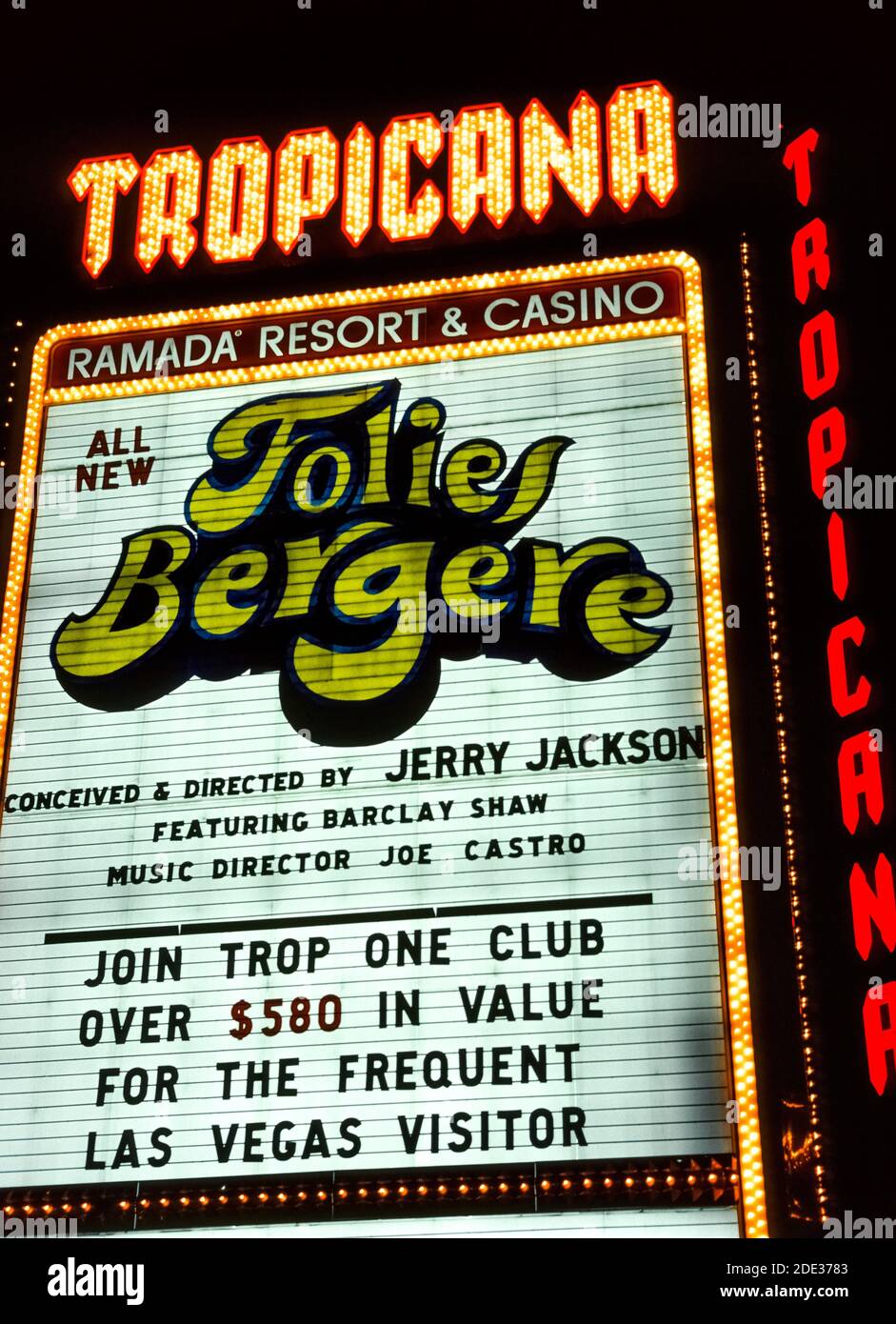 El neón y otras luces hicieron que este cartel al aire libre para el Tropicana Resort & Casino destaque por la noche a lo largo de las Vegas Boulevard, más conocido como el Strip, una carretera bordeada de espectaculares hoteles y casinos al sur de los límites de la ciudad de las Vegas, Nevada, Estados Unidos. El Tropicana abrió sus puertas en 1957 y ha estado operando desde entonces en ese famoso destino desértico conocido por sus juegos de azar y buenos tiempos. Esta fotografía histórica fue tomada en 1983 cuando el Tropicana era propiedad de la cadena hotelera Ramada. El letrero anuncia el entretenimiento del hotel, el espectáculo Folies Bergére. Foto de stock