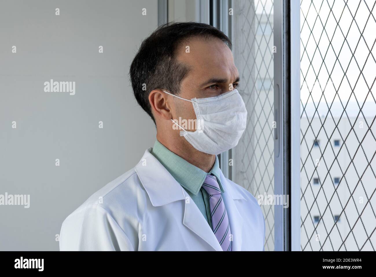 doctor de 44 años, sonriendo, en un abrigo blanco y corbata, mirando la cámara. Foto de stock