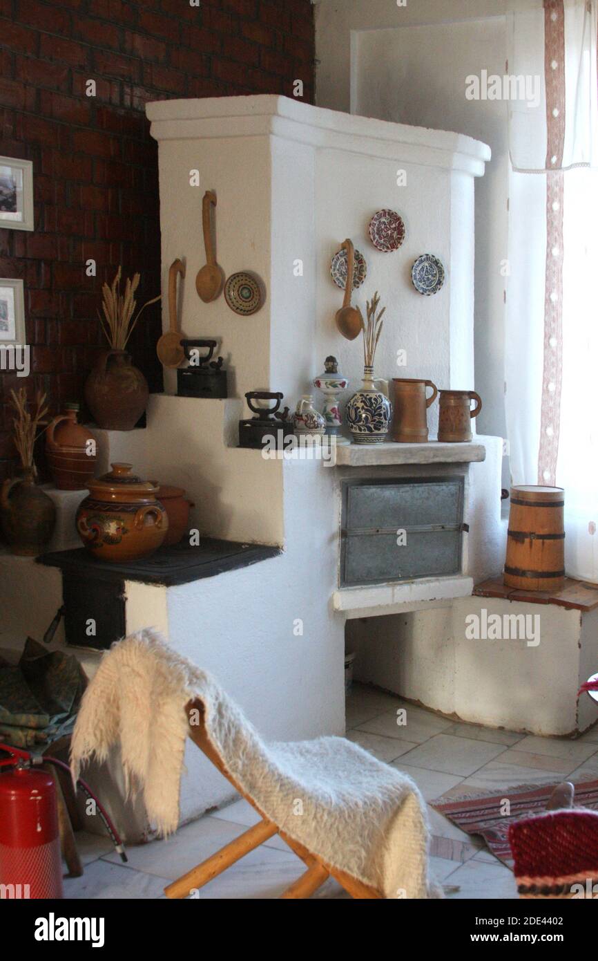 Condado de Buzau, Rumania. Interior con estufa de madera tradicional y calentador. Artículos folclóricos hechos a mano usados como decoración. Foto de stock