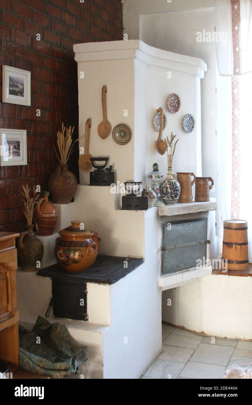 Condado de Buzau, Rumania. Interior con estufa de madera tradicional y calentador. Artículos folclóricos hechos a mano usados como decoración. Foto de stock