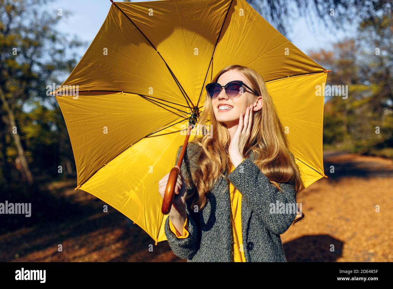 Chica joven feliz con abrigo con paraguas amarillo caminando en Park con  hojas amarillas, hora de otoño Fotografía de stock - Alamy