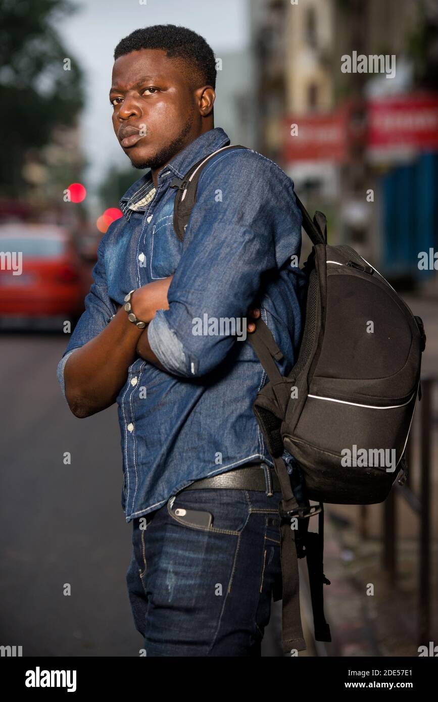 joven hombre de pie en mochila vaquera con brazos cruzados mirando hacia  los lados con cejas frunciendo el ceño Fotografía de stock - Alamy