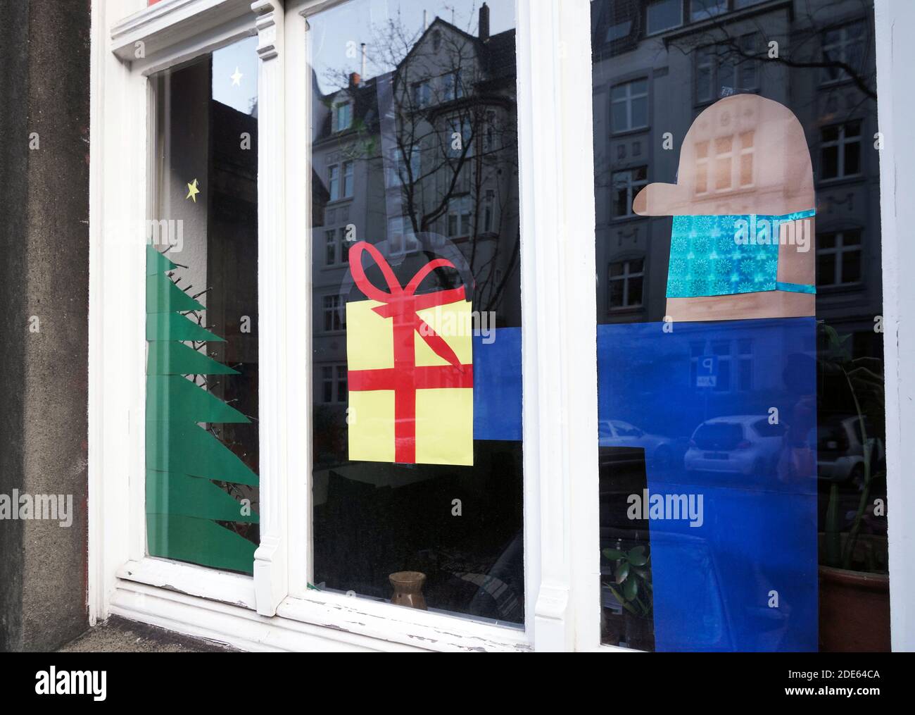 Dortmund, Alemania, 29 de noviembre de 2020: La ventana del apartamento decorada para Navidad se refiere a la víspera de Navidad en Corona Times. El hombre que da el regalo lleva la protección de la boca y la nariz contra el virus. Foto de stock
