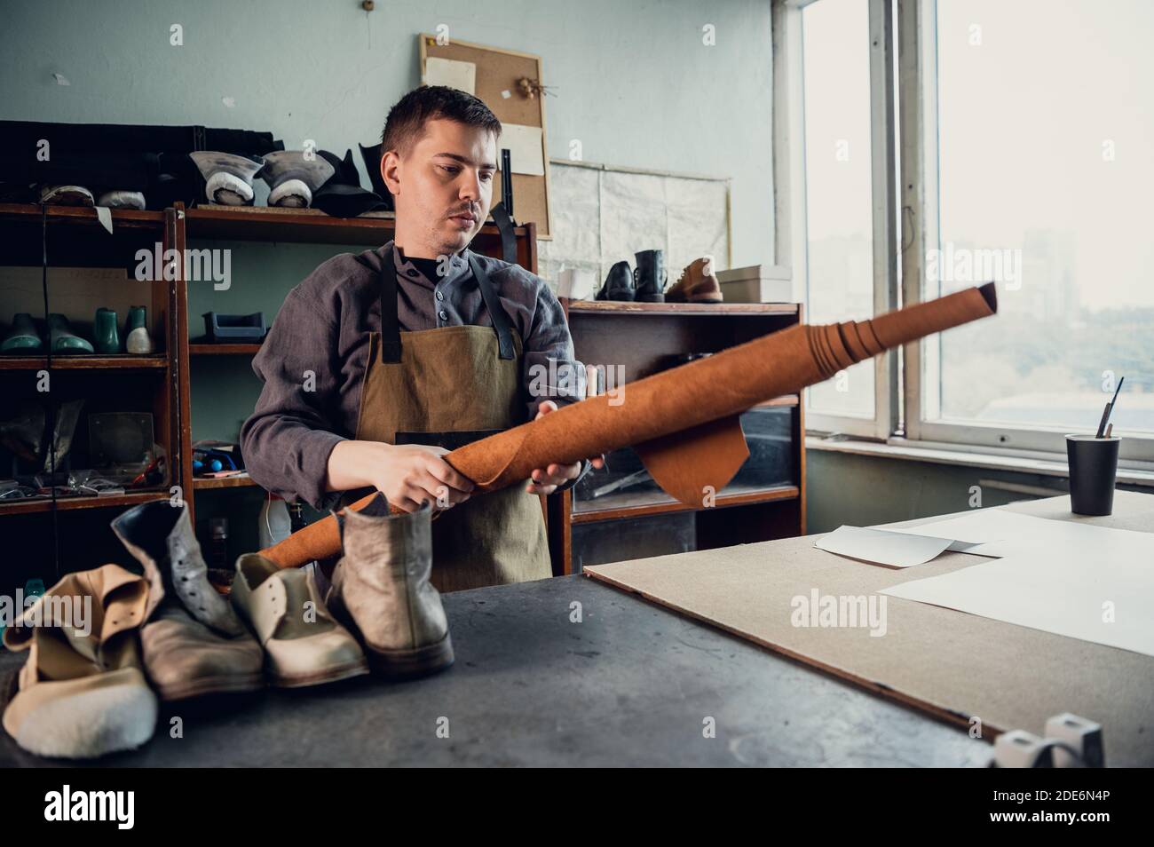 Un zapatero joven comienza a fabricar zapatos, pone un rollo de cuero en la  mesa Fotografía de stock - Alamy