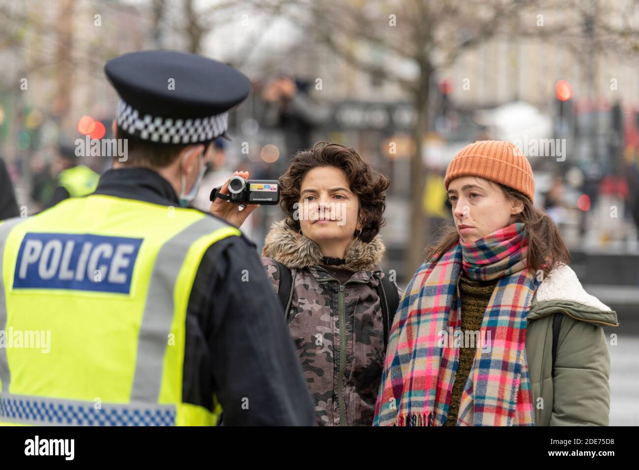 Mujeres blancas caucásicas filmando a un oficial de policía en una marcha de protesta contra el bloqueo del Coronavirus COVID 19 en Londres, Reino Unido. Uso de la cámara de vídeo Foto de stock