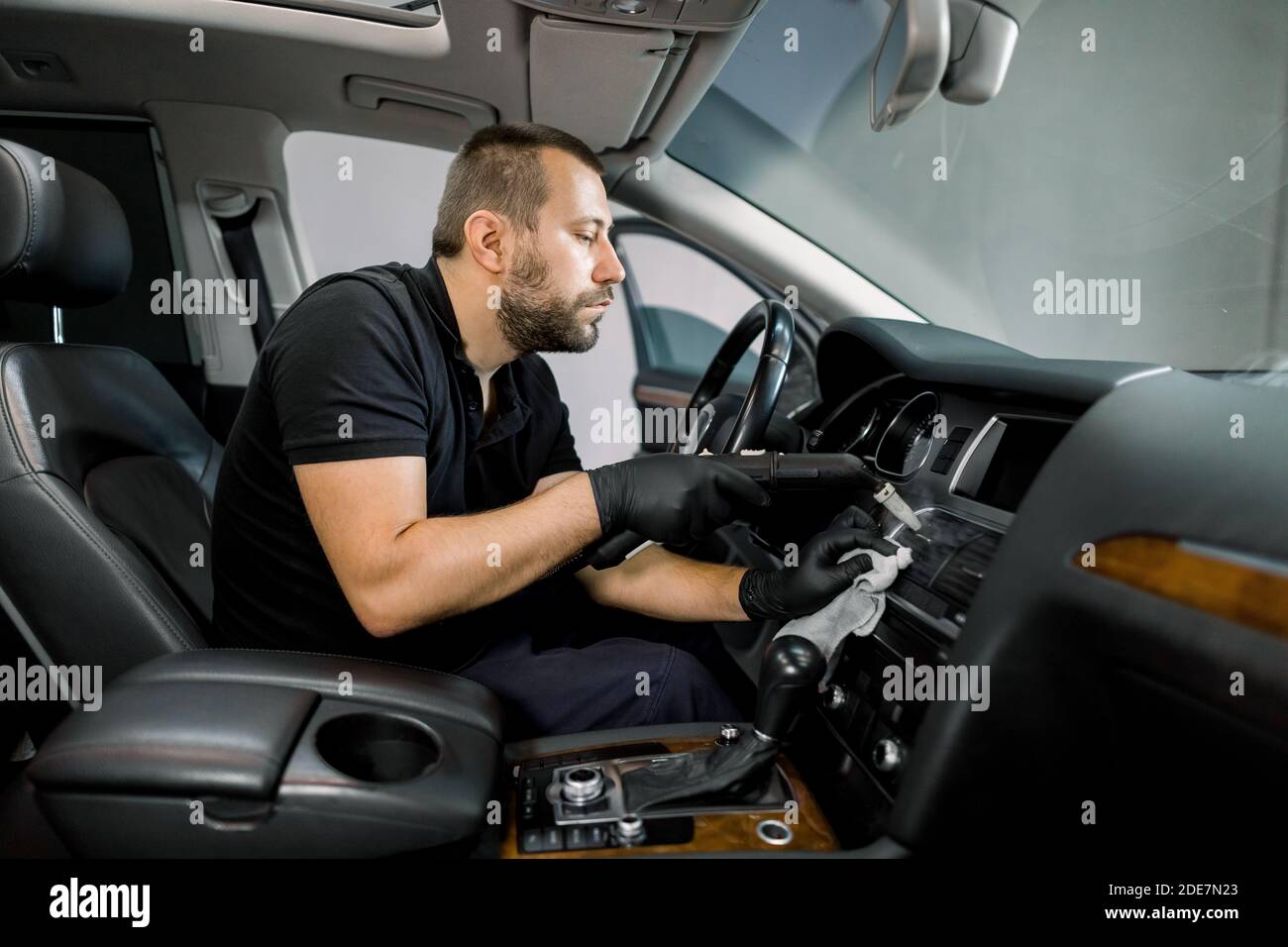 Servicio de limpieza del aire acondicionado del coche con vapor caliente.  Trabajador masculino caucásico profesional concentrado en uniforme negro,  sentado en el asiento delantero Fotografía de stock - Alamy