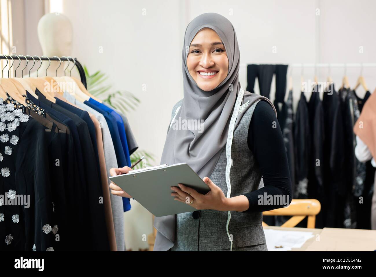 Feliz sonrisa mujer musulmana asiática diseñadora como un negocio de inicio propietario trabajando en su tienda de sastre Foto de stock