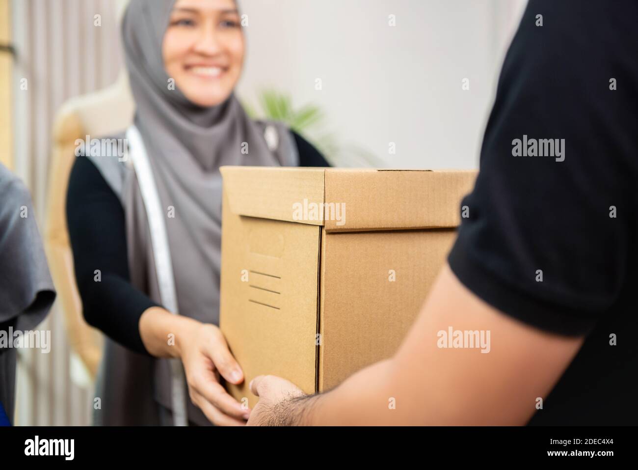 El hombre de la entrega dando la caja de la parcela a la diseñadora musulmana en su tienda de sastre Foto de stock