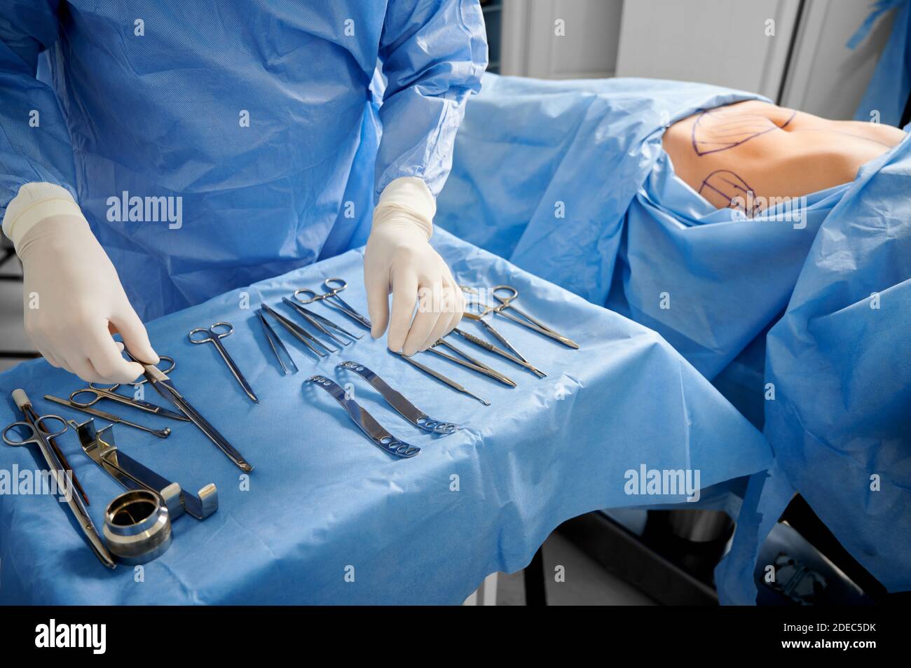 Primer plano de cirujano en guantes estériles preparando instrumentos  médicos. Paciente femenino con marcas en la piel tumbada en la cama médica  mientras el médico prepara las herramientas. Concepto de preparación de