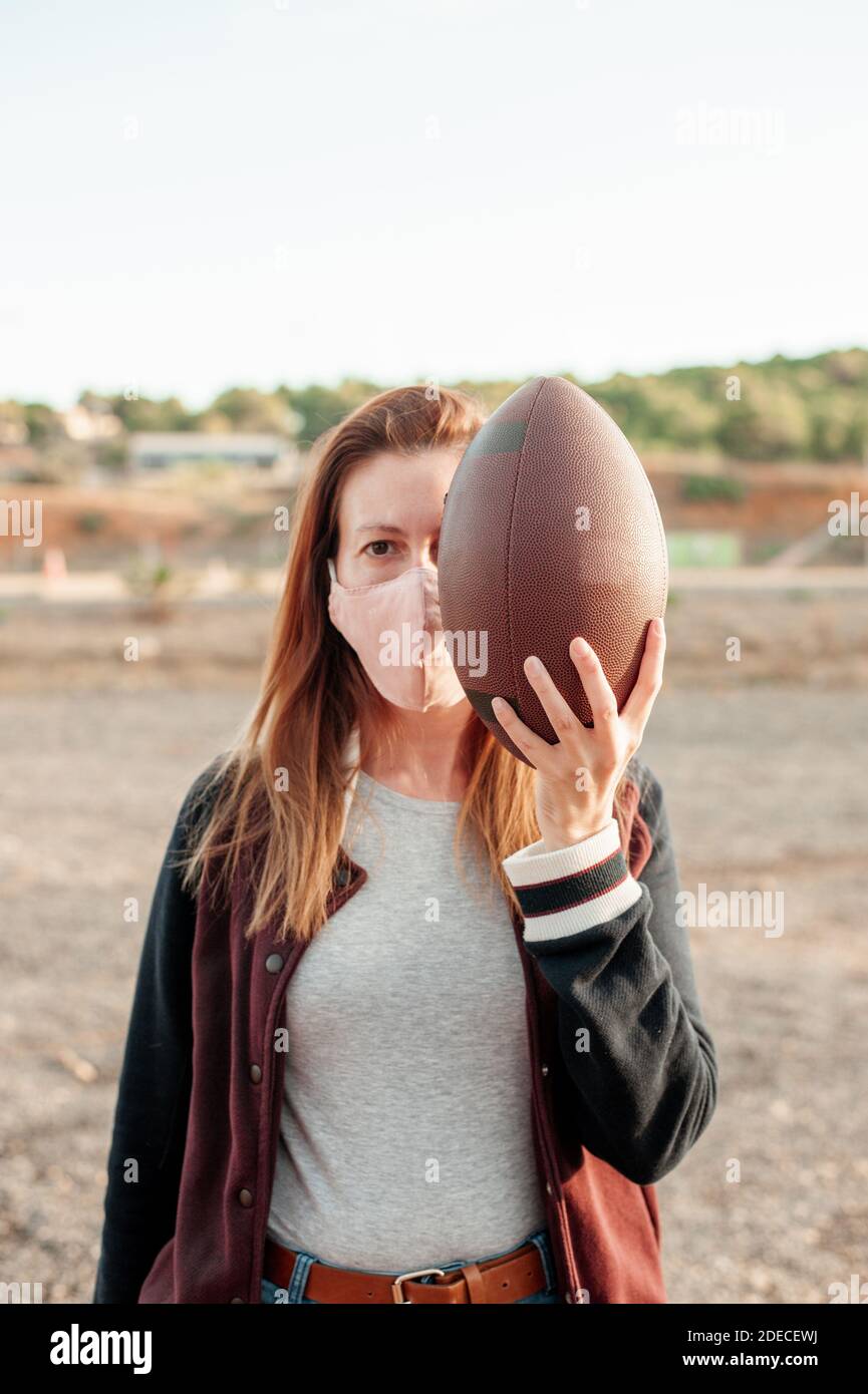 Mujer con máscara protectora sosteniendo una pelota de fútbol americano.  Nuevo concepto normal Fotografía de stock - Alamy