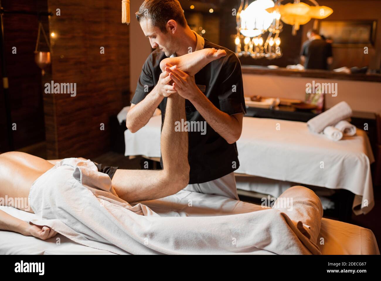 Terapeuta profesional haciendo un masaje profundo a un cliente masculino en el salón de Spa. Trabajando en la parte inferior del cuerpo Foto de stock