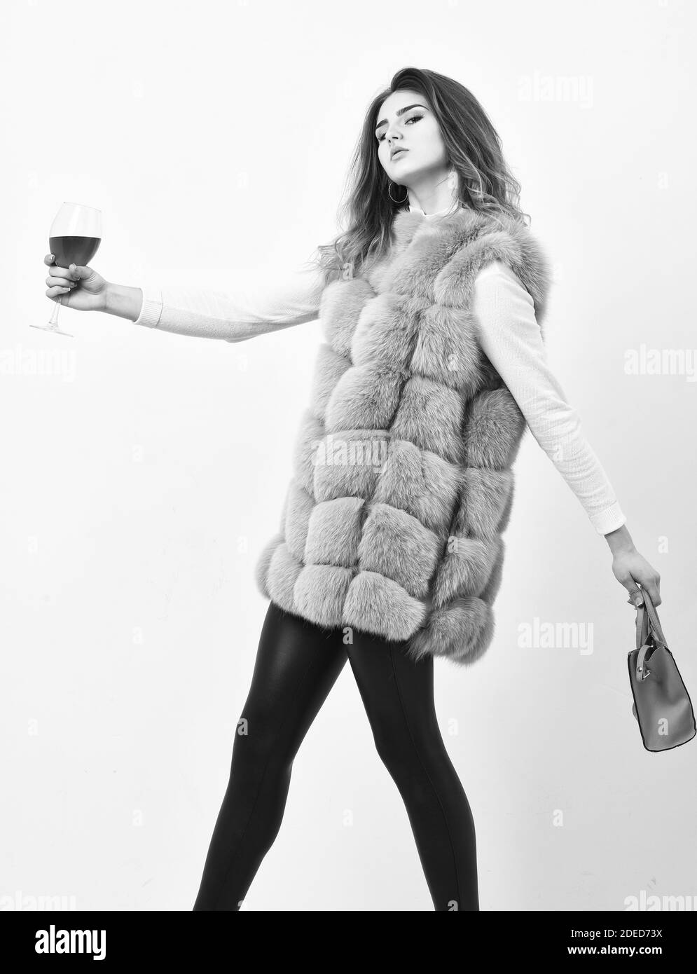 Mujer con bolso sostenga una copa de vino. Niña llevar chaleco de piel de moda mientras posan con bolsa. Concepto de tienda de lujo. A Lady le gusta compras. Ropa