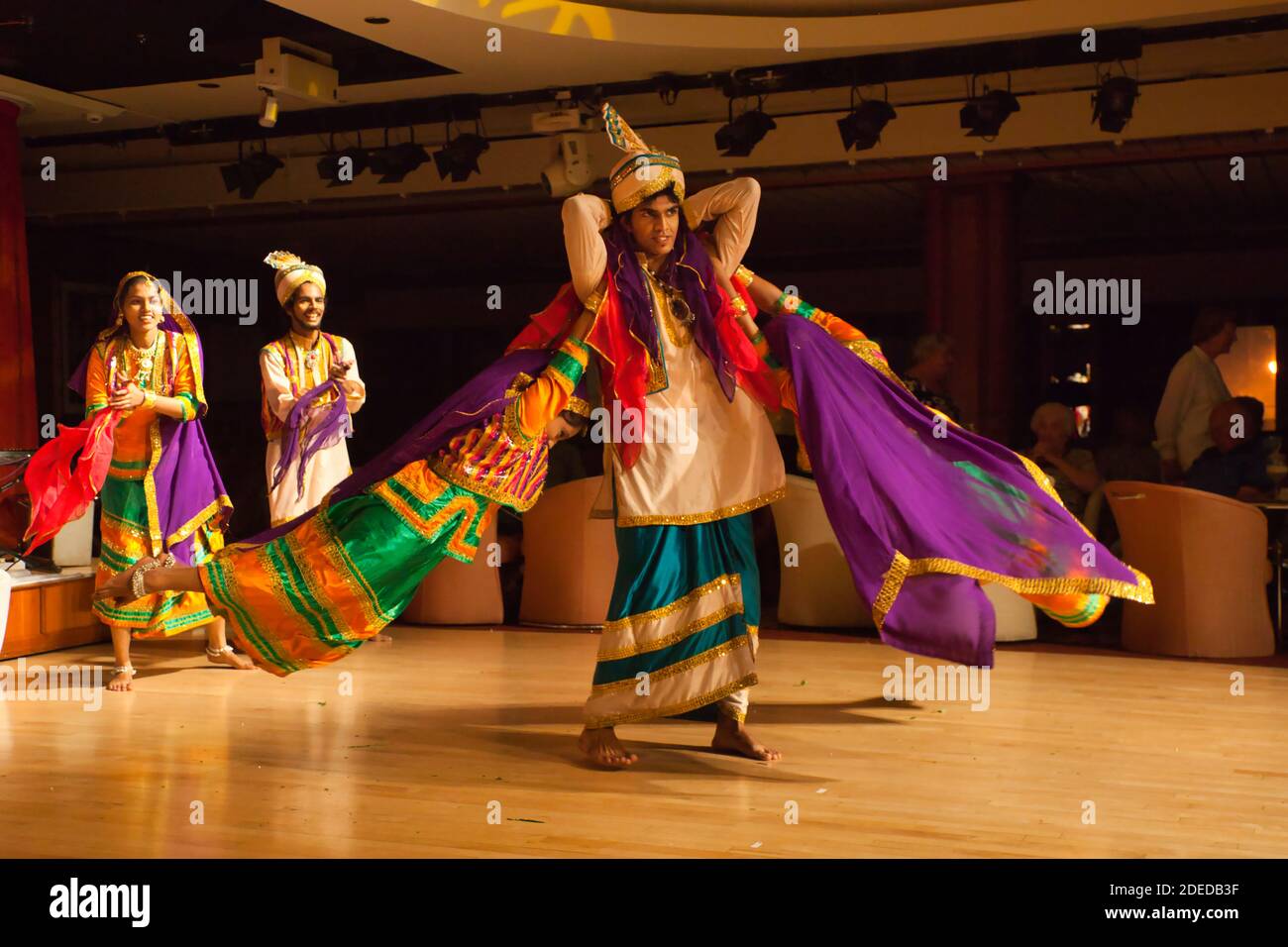Bailarines folklóricos dan una actuación en Mumbai, India y un bailarín masculino retuerce a dos bailarinas alrededor de él, todo en trajes coloridos Foto de stock
