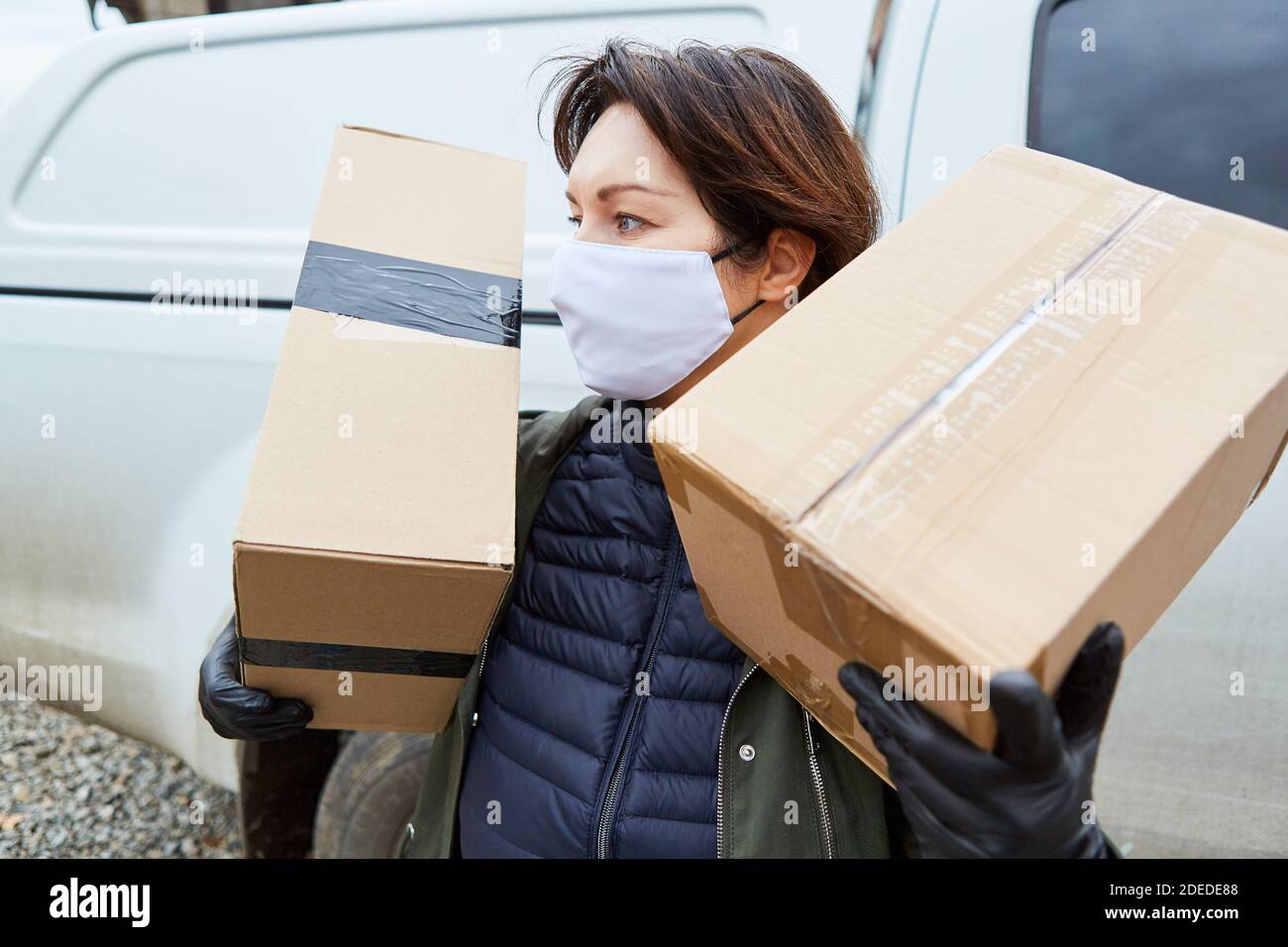 Servicio de entrega de transporte de paquetes con máscara y paquetes para la entrega está fuera Foto de stock