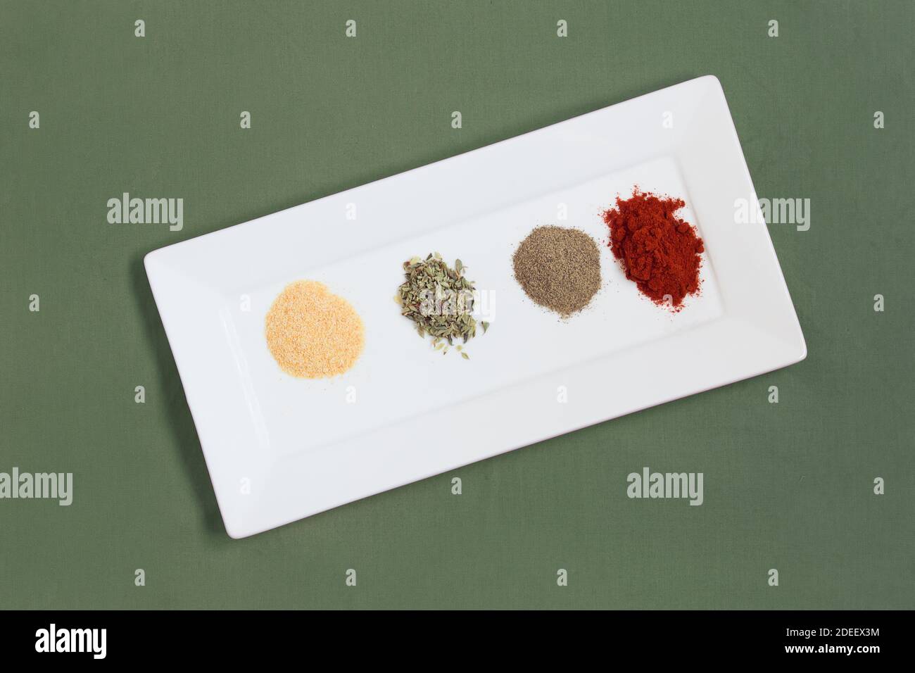 Una variedad de coloridas especias secas y en polvo en una bandeja blanca sobre una mesa con mantel de tela verde. Alimentos saludables y veganos. Foto de stock