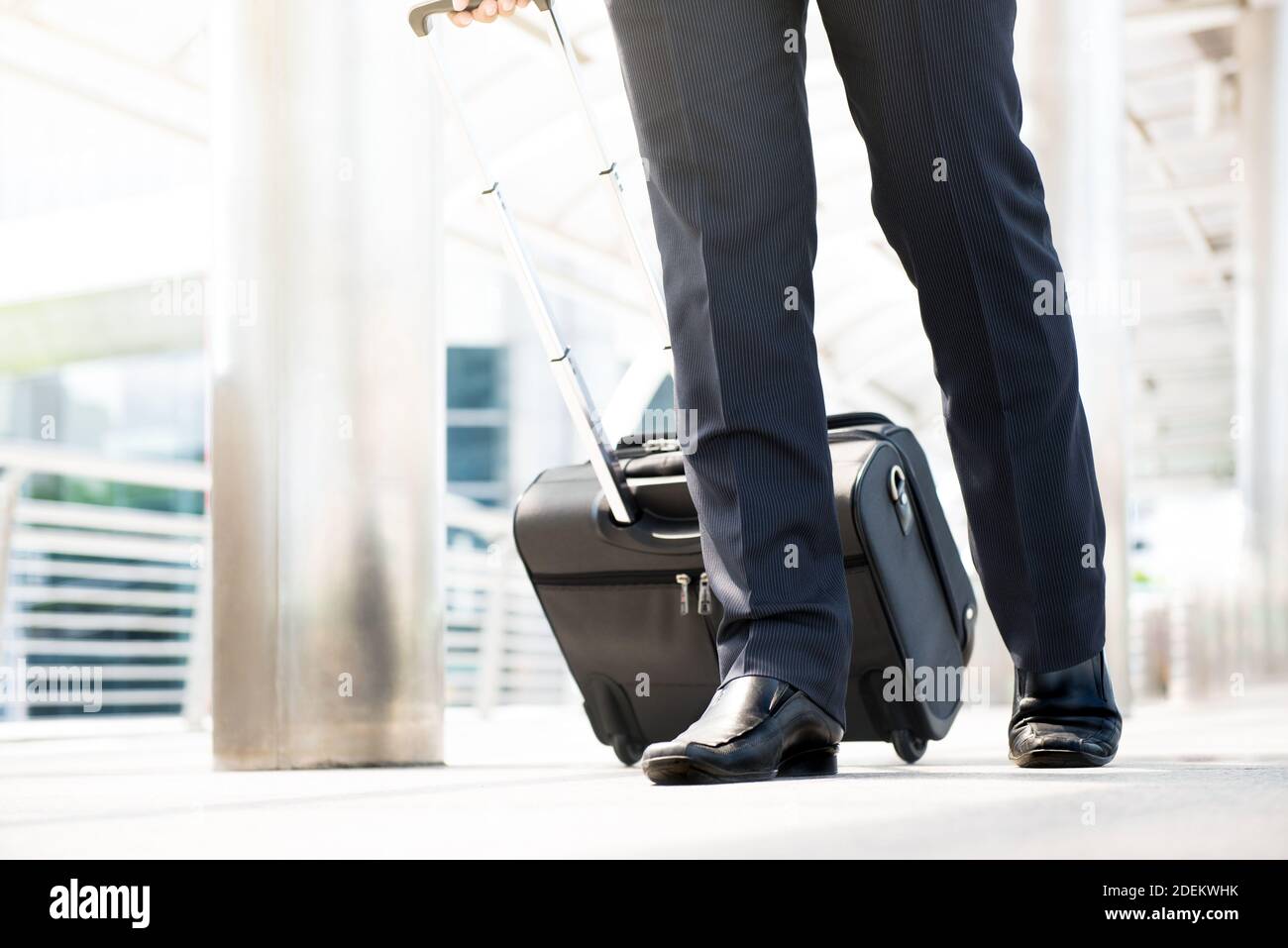Parte inferior de un hombre de negocios itinerante o mayordomo caminando y tirando equipaje en la pasarela exterior del aeropuerto Foto de stock
