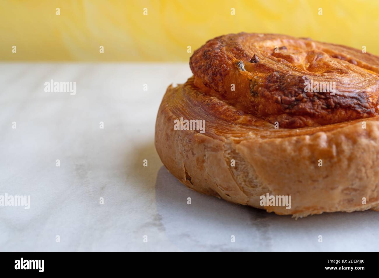 Vista lateral cercana de un solo pan de remolino de queso jalapeno sobre una encimera de mármol gris con una pared con textura amarilla en el fondo iluminado con nat Foto de stock