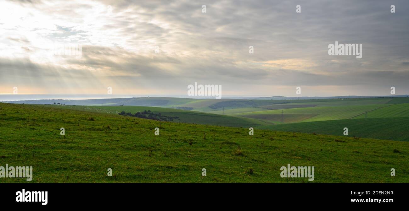 Vista sobre colinas onduladas y verdes al mar con luz solar suave e invernal desde South Downs Way en la zona de Devil's Dyke, West Sussex, Inglaterra. Foto de stock