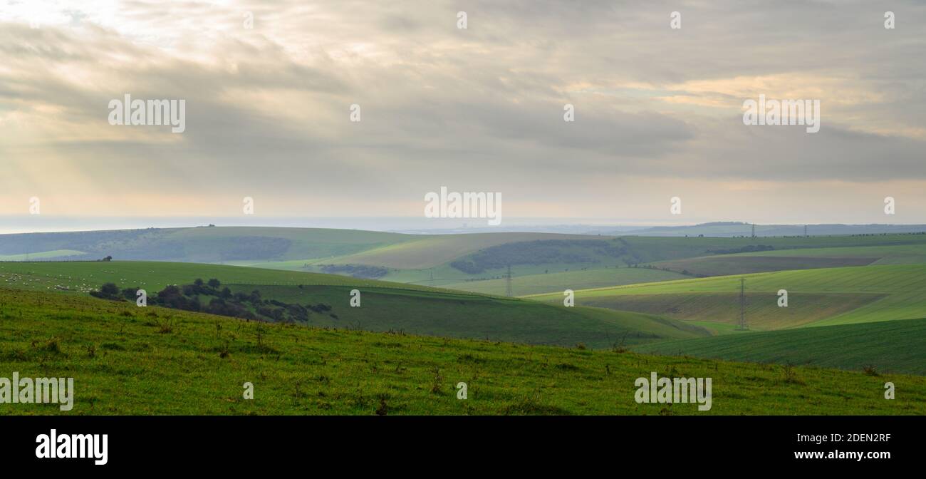 Vista sobre colinas onduladas y verdes al mar con luz solar suave e invernal desde South Downs Way en la zona de Devil's Dyke, West Sussex, Inglaterra. Foto de stock