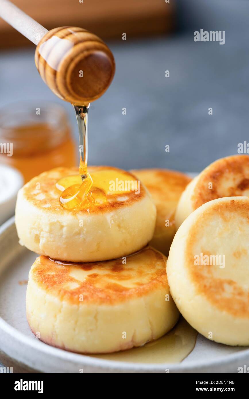 Miel vertiendo en el queso cottage panqueques fritters Syrniki Foto de stock