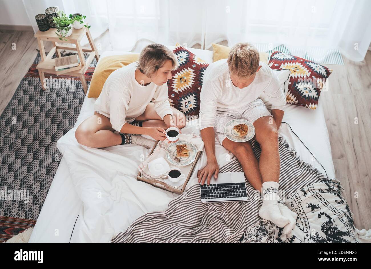 Los adolescentes se unen en pijamas en una cama acogedora navegando por Internet usando un ordenador portátil y tomando un café por la mañana con postre pastel de manzana. Parejas relaciones an Foto de stock