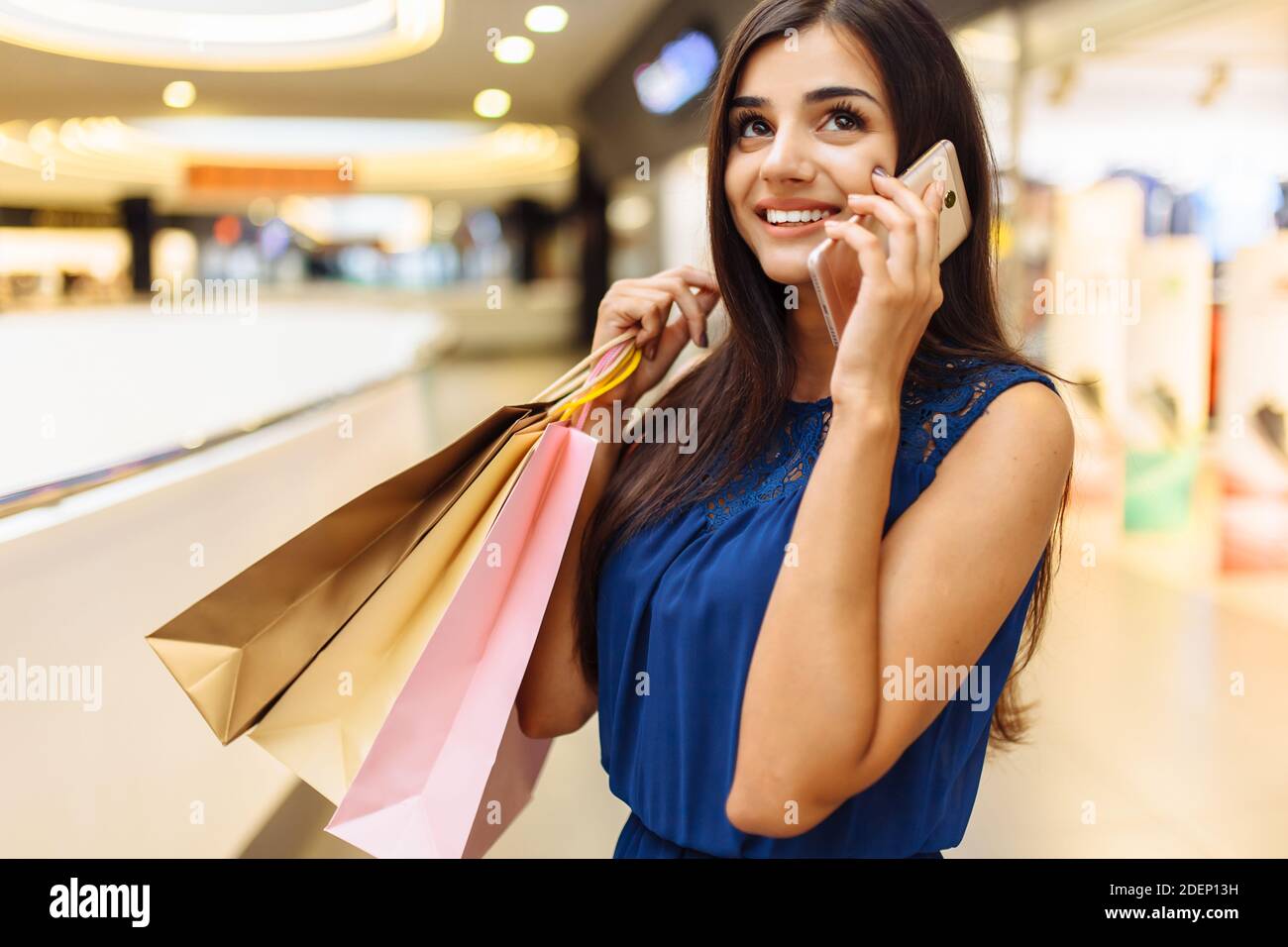 Chica hablando por teléfono mientras compras, retrato de una mujer con paquetes en la tienda Foto de stock