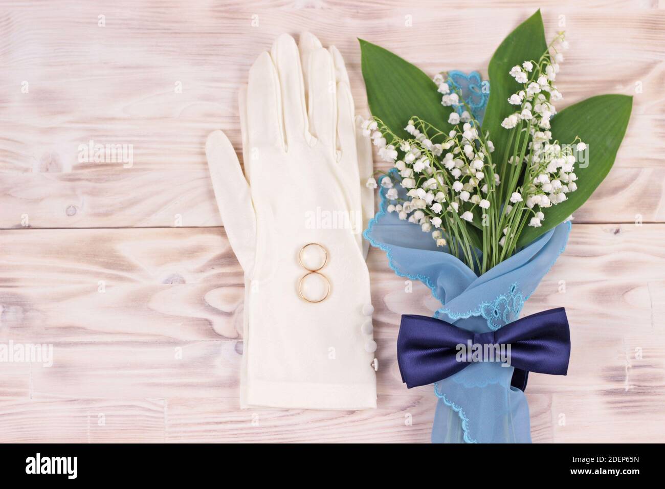 Ramo de flores lirio del valle en servilleta de color turquesa, guantes blancos de boda femenina y lazo azul en mesa rústica ligera.Tarjeta de felicitación de boda Foto de stock