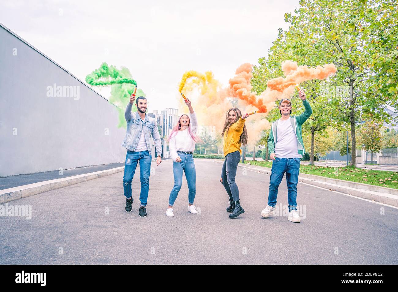 Gente joven sonriente feliz corriendo en la calle con un color Señal cohete en la mano - Feliz concepto de amistad con jóvenes estudiantes que se divierten toget Foto de stock