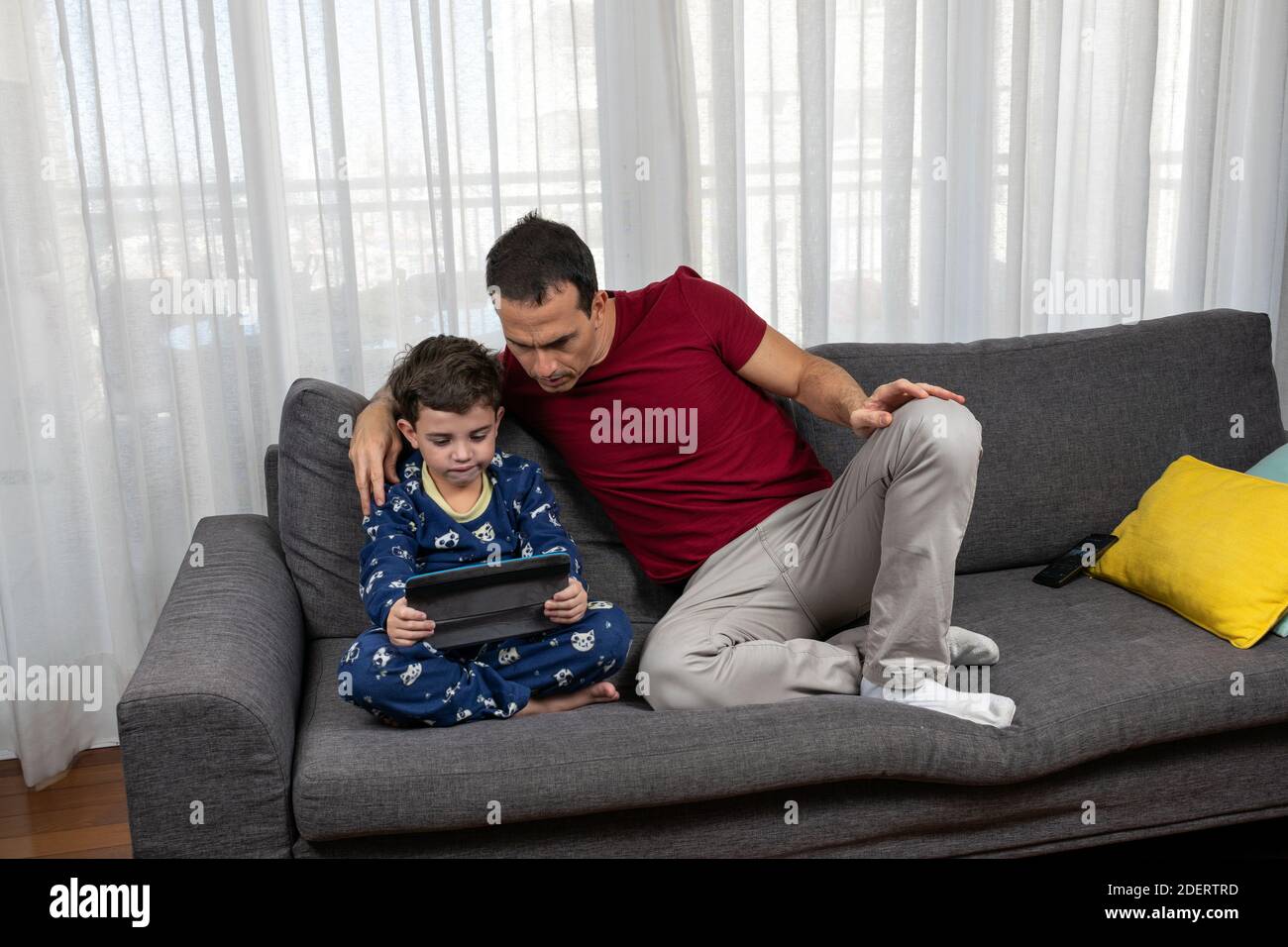 Hombre maduro (44 años) sentado junto a su hijo (6 años) viendo una película juntos. Foto de stock