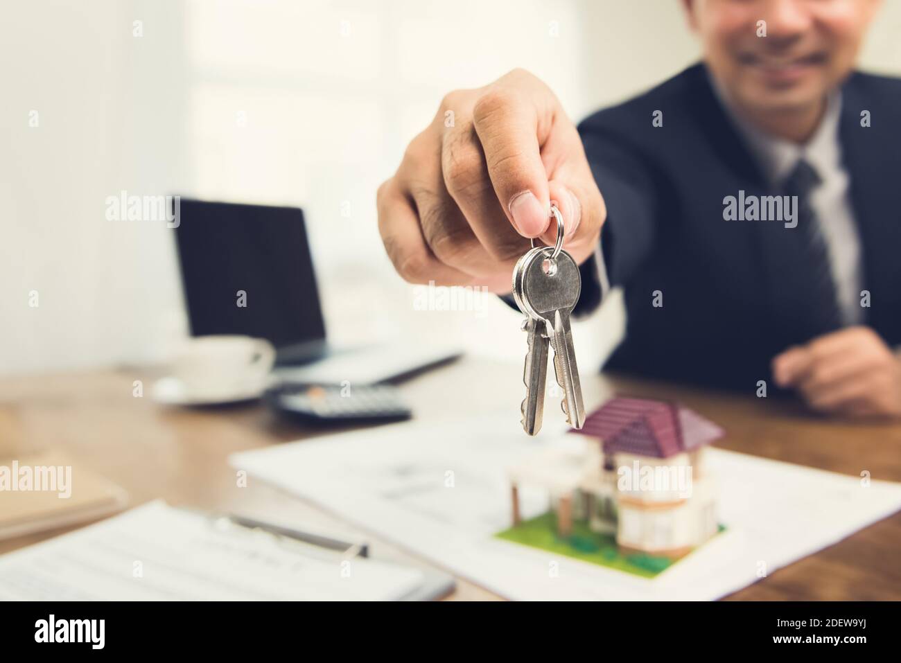 Hombre de negocios sonriente como agente de bienes raíces givng casa las llaves de su escritorio en la oficina Foto de stock