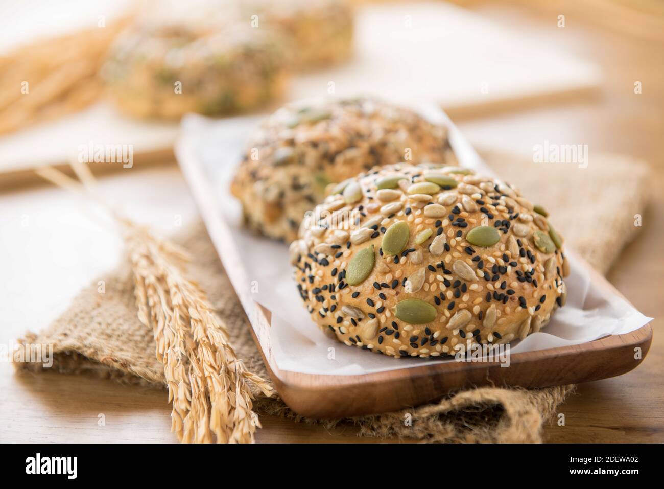 Granos de pan sanos de semillas de cereal mezclado multigrano en placa de madera mostrar con textura de saco de yute marrón en la mesa Foto de stock