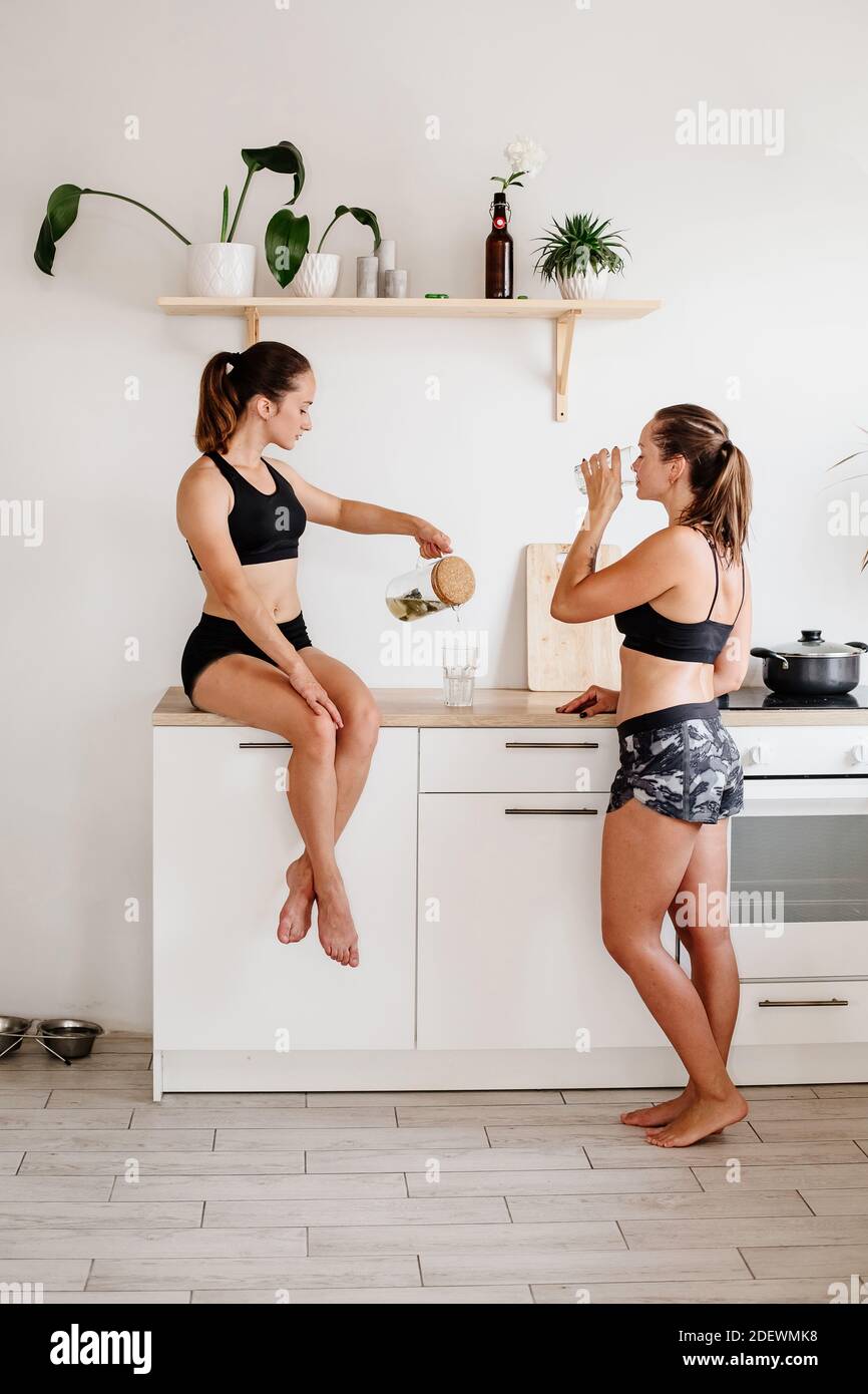 Dos chicas deportivas pasan tiempo en la cocina. Las mujeres en shorts  deportivos y tops están sentadas en los muebles de cocina y la limonada de  beber Fotografía de stock - Alamy