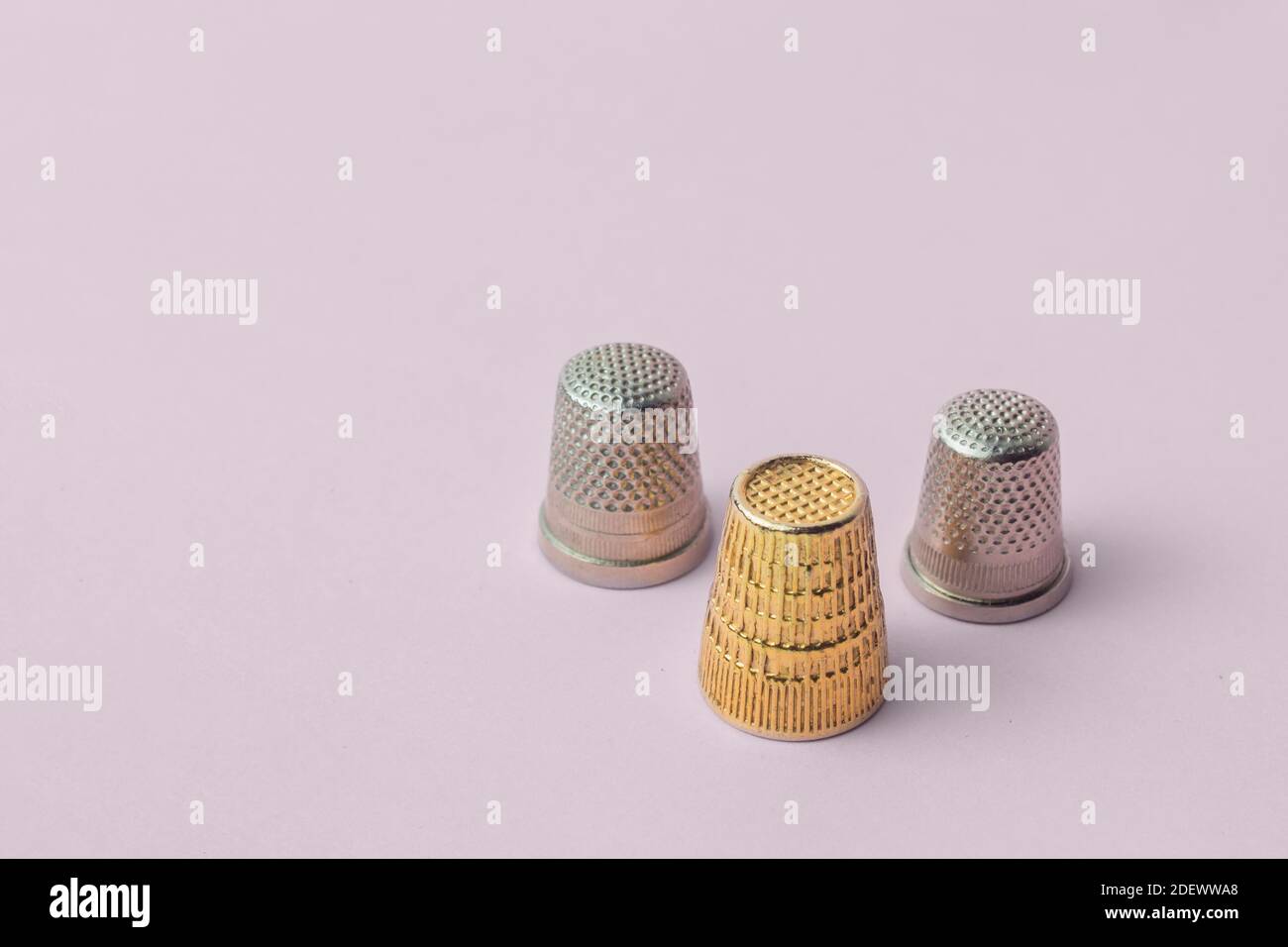 Composición triangular de tres dedales, dos tipos, y un oro sobre fondo rosa. Artículos de costura. Foto de stock