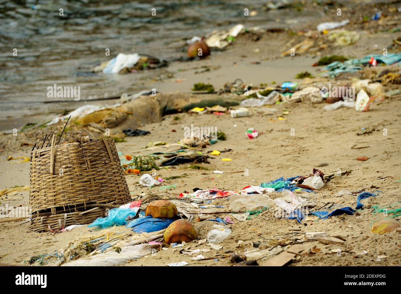 Los objetos arrojados por el mar varados en una playa de arena en Vietnam. Cesta trenzada en primer plano, bolsas de plástico, basura y el mar de fondo. Foto de stock