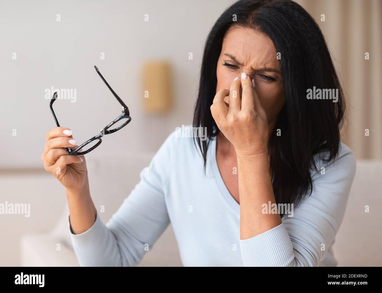 Mujer madura cansada masajeando el puente nasal en casa Foto de stock